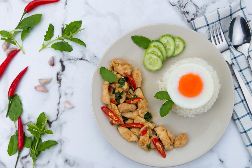 Close-up of a Thai basil chicken dish with rice and a sunny-side-up egg, styled with fresh ingredients.