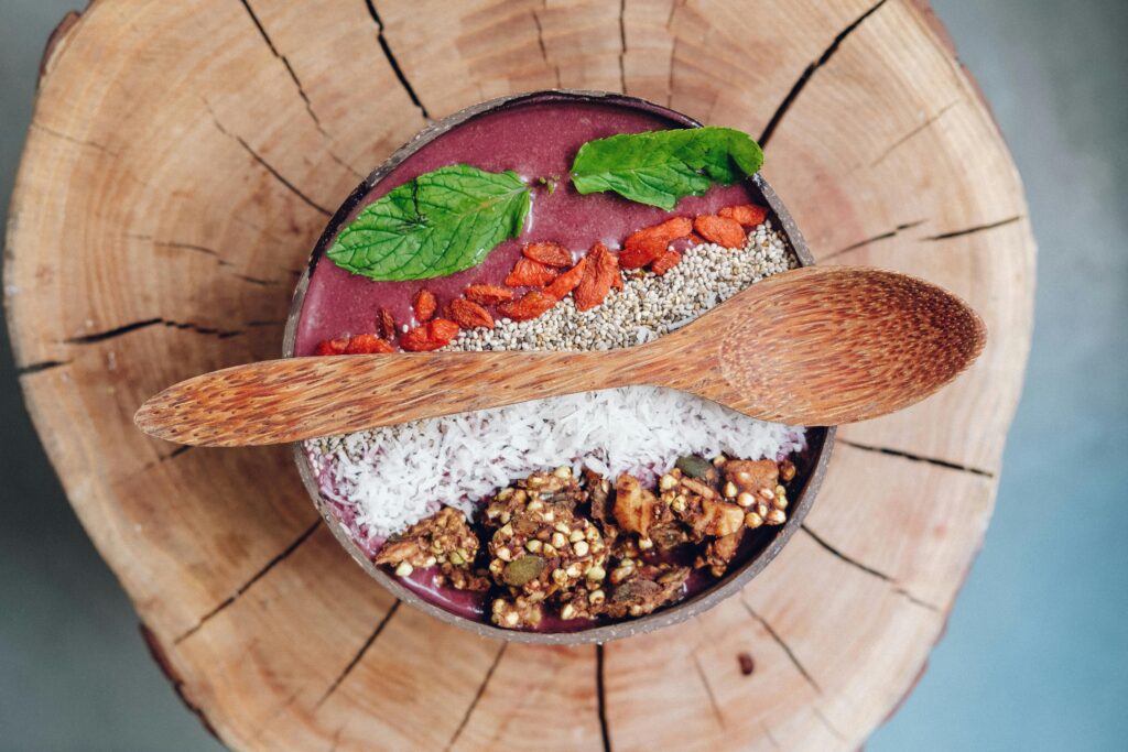 Healthy acai bowl with granola, mint leaves, and berries served on rustic wood.