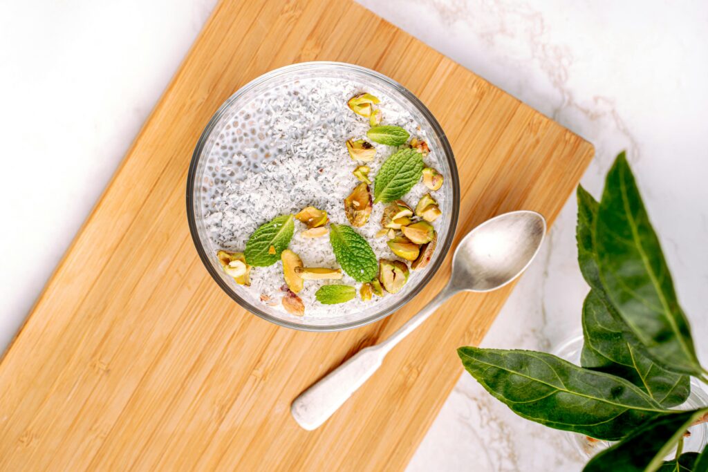 pexels-photo-5589029-5589029 Top view of a chia seed pudding bowl garnished with pistachios and mint leaves on a wooden board.