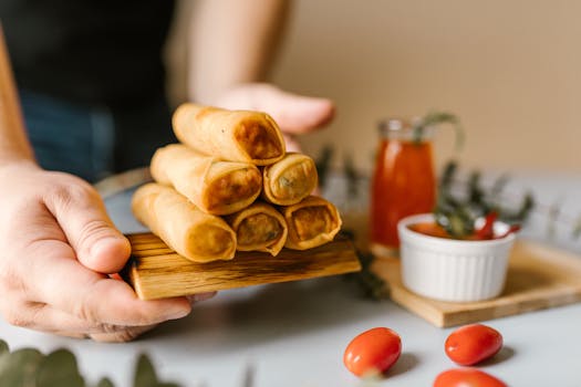 pexels-photo-6646369-6646369 Close-up of crispy spring rolls served with dipping sauce and garnishes.