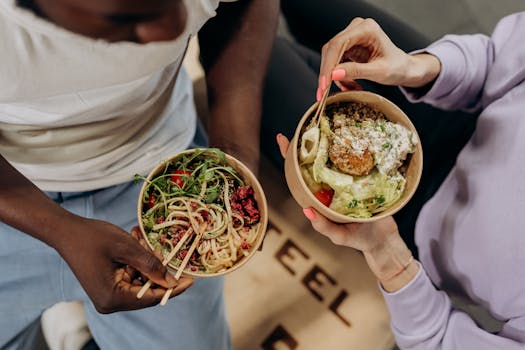 pexels-photo-6740535-6740535 Two people holding bowls filled with salad and pasta, emphasizing healthy lifestyle choices.