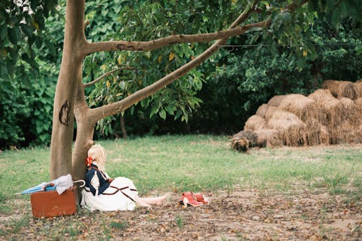 A woman rests under a tree beside her suitcase in a serene outdoor setting.