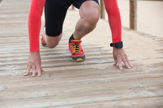 Athlete in red gear gets ready to sprint on a wooden path in sunny outdoor setting.